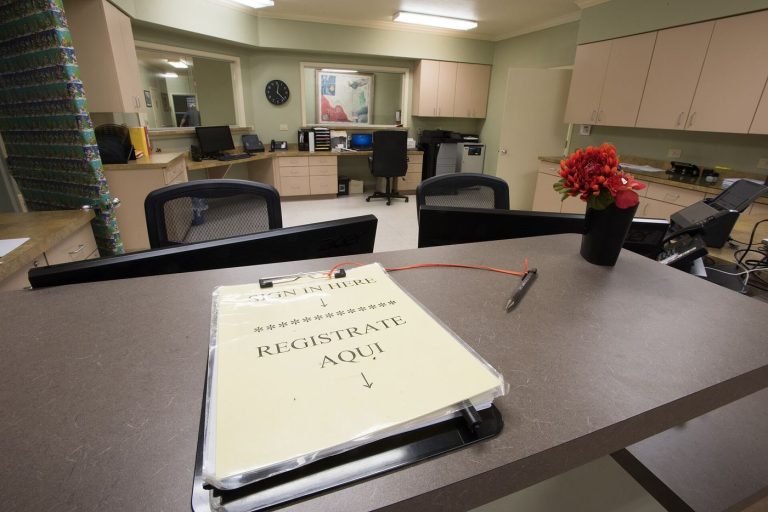 Patients sitting in a bright community clinic waiting room with chairs and a reception desk.