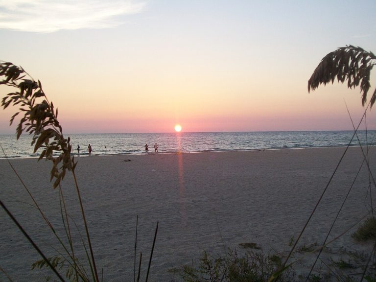 Sunset over a Gulf of Mexico beach with calm water and shoreline grasses